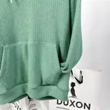 Canguro verde de tejido waffle con capucha, cordones blancos, bolsillo tipo canguro y logo bordado en blanco en el pecho.