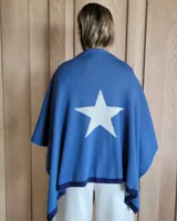 Ruana de tejido de punto en color crema con detalle de estrella grande en color verde lima en la espalda y bordes en tono arena.