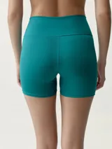 Short deportivo ajustado de tiro alto, color verde azulado, con pequeño logo estampado en la pierna izquierda.