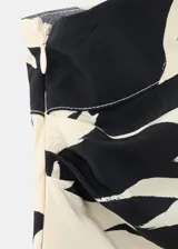 Mono largo de viscosa con diseño bicolor en negro y beige con estampado de hojas tropicales. Presenta un corte asimétrico de un solo hombro con manga larga holgada, pantalón de silueta recta y lazo ajustable en la cintura.