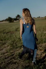 Vestido tejido en lurex color plateado, con diseño geométrico en cuero en el frente y flecos en el ruedo. Breteles finos de cuero con tientos plateados.