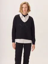 Buzo de lana negro con cuello en V y diseño de rombos calados en el frente. Se lleva superpuesto a una camisa de color claro.