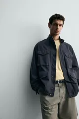 Cazadora regular fit de algodón color gris oscuro con efecto lavado, cuello subido, manga larga y cierre frontal con cremallera oculta por solapa con botones a presión. Cuenta con cuatro bolsillos frontales de plastrón con solapa y cintura ajustable con cordón interior.