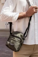 Morral color verde militar con varios bolsillos, cierre principal y bolsillo frontal con cierre. Incluye correa ajustable de tela negra y parche con texto "NOT JUST A BAG".