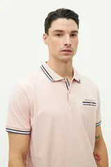 Remera polo rosada de manga corta, con cuello y puños acanalados con rayas blancas, azules y negras. Tiene un bolsillo en el pecho con el logo "BROOKSFIELD" bordado y un botón rosado.