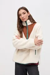 Buzo de sherpa color marrón con diseño de medio cierre frontal. Presenta un panel superior en forma de V en color beige y detalles de vivos en color fucsia en el cierre, cuello y bolsillos laterales. Cuenta con cuello alto y bolsillos frontales.