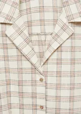 Blusa de algodón con diseño de cuadros, cuello camisero, manga corta y cierre frontal con botones. Presenta un diseño corto con detalle de lazo para anudar en la cintura.