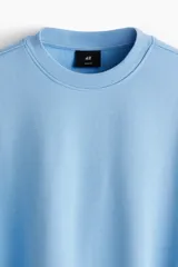 Buzo azul claro de tejido de mezcla de algodón, con interior cepillado suave, cuello redondo ribeteado, hombros caídos y remate acanalado ancho en puños y bajo. Corte holgado.