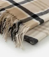 Bufanda de punto suave con estampado de cuadros en tonos beige, blanco y negro, con terminaciones de flecos en los extremos.