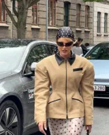 Chaqueta estructurada color beige con cuello, ribetes de bolsillos y detalles en negro. Presenta un diseño entallado con cierre frontal completo y hombreras marcadas.