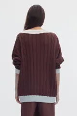 Sweater de punto oversized de color marrón, con escote en V, detalles de ochos y puños, cuello y ruedo en tono celeste y blanco.