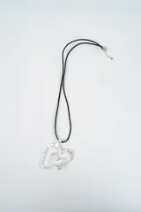 Collar con dije de doble corazón en metal plateado, con textura martillada en el corazón exterior y superficie lisa en el interior, montado sobre un cordón negro ajustable.