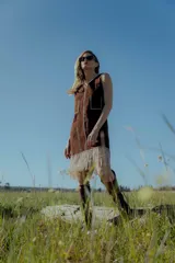 Vestido corto negro sin mangas, con escote en V y detalle de flecos en el ruedo. Presenta bordados en color blanco en el escote, los bolsillos y el centro del vestido.