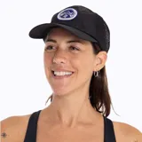 Gorra tipo trucker de color negro con paneles laterales y traseros de malla. Presenta un parche circular bordado en el panel frontal con el logo de Merrell y un diseño de montañas.