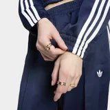 Campera deportiva Adidas de satén color azul marino, con cierre frontal y cuello tipo bomber. Presenta las icónicas tres tiras blancas en las mangas y el logo del trifolio bordado en el pecho.
