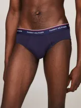 Pack de tres calzoncillos tipo slip de la marca Tommy Hilfiger, confeccionados en algodón elástico, con cintura elástica con el nombre de la marca y líneas distintivas. Incluye una unidad con cintura blanca, otra con cintura azul marino y otra con cintura roja.
