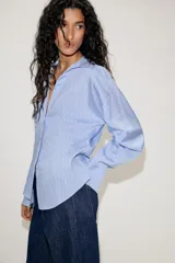 Camisa de manga larga con cuello solapa y escote en pico. Presenta un diseño entallado en la cintura y cierre frontal mediante botones.