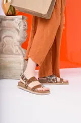 Sandalia negra de plataforma gruesa con dos tiras anchas ajustables con hebilla. Una de las tiras tiene un estampado de vaca blanco y negro.