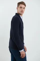 Cardigan tejido color azul marino, con cuello y solapa, cierre frontal de botones y bolsillos delanteros. Presenta un tejido de punto con textura.