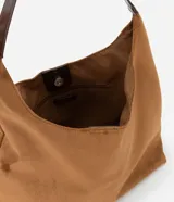 Cartera tipo hobo de gran tamaño confeccionada en material sintético efecto gamuza color tostado. Presenta una estructura flexible, asa única en tono contrastante y cierre mediante botón a presión.