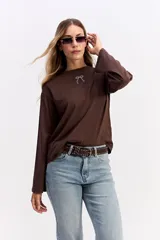 Remera de manga larga color beige con silueta relajada y mangas amplias. Presenta una estampa en la espalda con la frase 'Be kind to your mind' acompañada de ilustraciones de un cupido, flores y lazos en tono bordó.