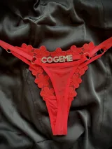 Tanga regulable de color rojo confeccionada en encaje con diseño floral y detalles de tul, con tiras ajustables mediante arandelas metálicas y detalle de letras plateadas con strass en la parte frontal.