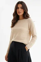Sweater de punto color beige claro, con cuello redondo y mangas largas. Presenta un tejido acanalado horizontal en el cuerpo y acanalado vertical en las mangas.