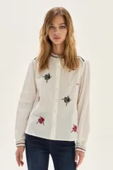 Camisa de algodón color crudo con cuello mao y cierre frontal de botones. Presenta bordados florales en tonos rojo y negro distribuidos en el cuerpo, cuello y puños.