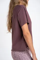 Remera deportiva color malva/ciruela, de manga corta y corte holgado, con cuello redondo y aberturas laterales en el ruedo.