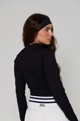 Top deportivo negro de manga larga, confeccionado en tejido acanalado, con cuello alto y cierre frontal parcial. Presenta un diseño ajustado tipo crop top con el logo 'bk.' estampado en el frente.