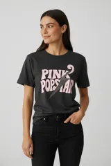 Remera de algodón color gris oscuro, con cuello redondo y mangas cortas. Presenta un estampado frontal con la frase 'PINK POPSTAR' en letras rosadas y un rayo central decorado con strass.