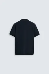 Jersey de punto color verde oliva, de calce relajado (relaxed fit), con cuello solapa y abertura frontal en forma de V. Es de manga corta y presenta acabados en rib en puños y ruedo.