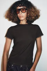 Camiseta de manga corta color marrón oscuro con textura acanalada, cuello redondo y bajo recto. Presenta un bajo superpuesto de tul o tela más clara, visible en el ruedo y en el cuello.