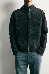 Chaqueta cropped fit de denim de algodón en color negro con efecto lavado, cuello mao y cierre frontal con cremallera. Presenta aplicaciones de trabillas horizontales en el pecho y en las mangas, además de hombreras abotonadas.