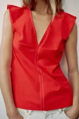Top rojo de popelín con escote en V pronunciado, mangas sisa y pespuntes en contraste. Cuenta con tirantes finos cruzados y lazada en la espalda.