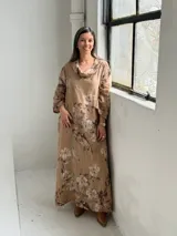Vestido largo de lino color camel con estampado floral en tonos marrón y crudo, cuello drapeado y mangas largas holgadas.