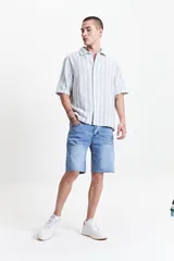 Bermuda de jean en fit relajado, color azul claro con efecto lavado. Presenta diseño de cinco bolsillos, cierre frontal con botón y bragueta, y terminación de basta cruda deshilachada.