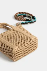 Cartera Rapsodia tipo tote mini en color tostado, confeccionada con cuerpo de tejido estilo red y detalles en material sintético liso. Cuenta con asas de mano acolchadas y una correa desmontable trenzada en tonos verde, rosa y marrón con herrajes metálicos. Incluye una placa frontal con el nombre de la marca grabado.