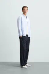 Camisa celeste a rayas verticales, de corte relaxed fit, confeccionada en lino y algodón. Tiene cuello abotonado, manga larga con puños abotonados, bolsillo de parche en el pecho y cierre frontal con botones.