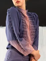 Chaqueta entallada de algodón tipo seda, teñida a mano con técnica tie-dye en tonos azul y naranja. Tiene cuello mao, mangas largas con puños abullonados y cierre frontal con broches.