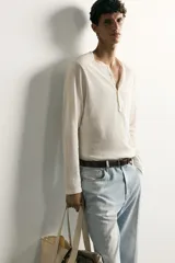 Remera polo de manga larga y calce regular fit en color blanco off-white, confeccionada en mezcla de algodón y lino, con cuello redondo y cartera con botonadura frontal.