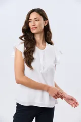 Blusa blanca sin mangas con volados en los hombros, cuello redondo con aberturas y cierre frontal parcial con botones.
