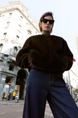 Chaqueta bomber de cuello redondo y manga larga, confeccionada en tejido de pelo sintético color marrón oscuro. Presenta cierre frontal con cremallera, bolsillos laterales y acabados elásticos en el ruedo y puños.