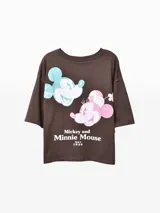 Remera oversize de manga corta color marrón oscuro, con diseño estampado de Mickey y Minnie Mouse al frente en tonos celeste y rosado.