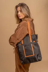 Bolso tipo tote bag de símil cuero color rosa pálido, con asas dobles y detalles de costura en color beige claro. Presenta un bolsillo frontal rectangular aplicado y herrajes metálicos.