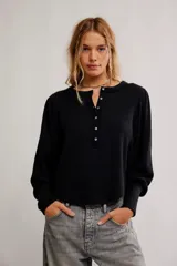 Top de tela con textura tipo gofrado, color negro, con escote redondo, botonadura henley y mangas largas abullonadas con puño.