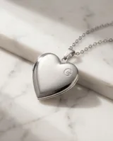Relicario de acero en forma de corazón con acabado pulido brillante, suspendido de una cadena de eslabones finos.