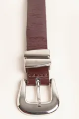 Cinturón de cuero liso color marrón oscuro con hebilla plateada y pasador metálico decorativo.