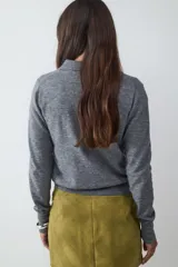Suéter tejido de punto color gris, con cuello polo y escote en V con un botón. Tiene mangas largas y está confeccionado en un tejido suave y liviano.