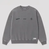 Buzo oversize de cuello redondo en color gris, con diseño estampado en el frente que incluye logotipos y texto. Presenta puños y ruedo acanalados, con una pequeña etiqueta decorativa en la parte inferior.